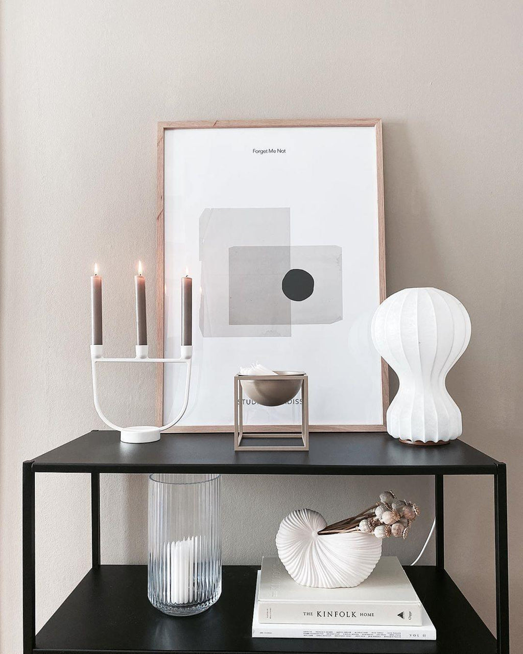 Clérachic lamp on a black metal console, beside a white candelabra, a framed abstract print and a ribbed glass vase.