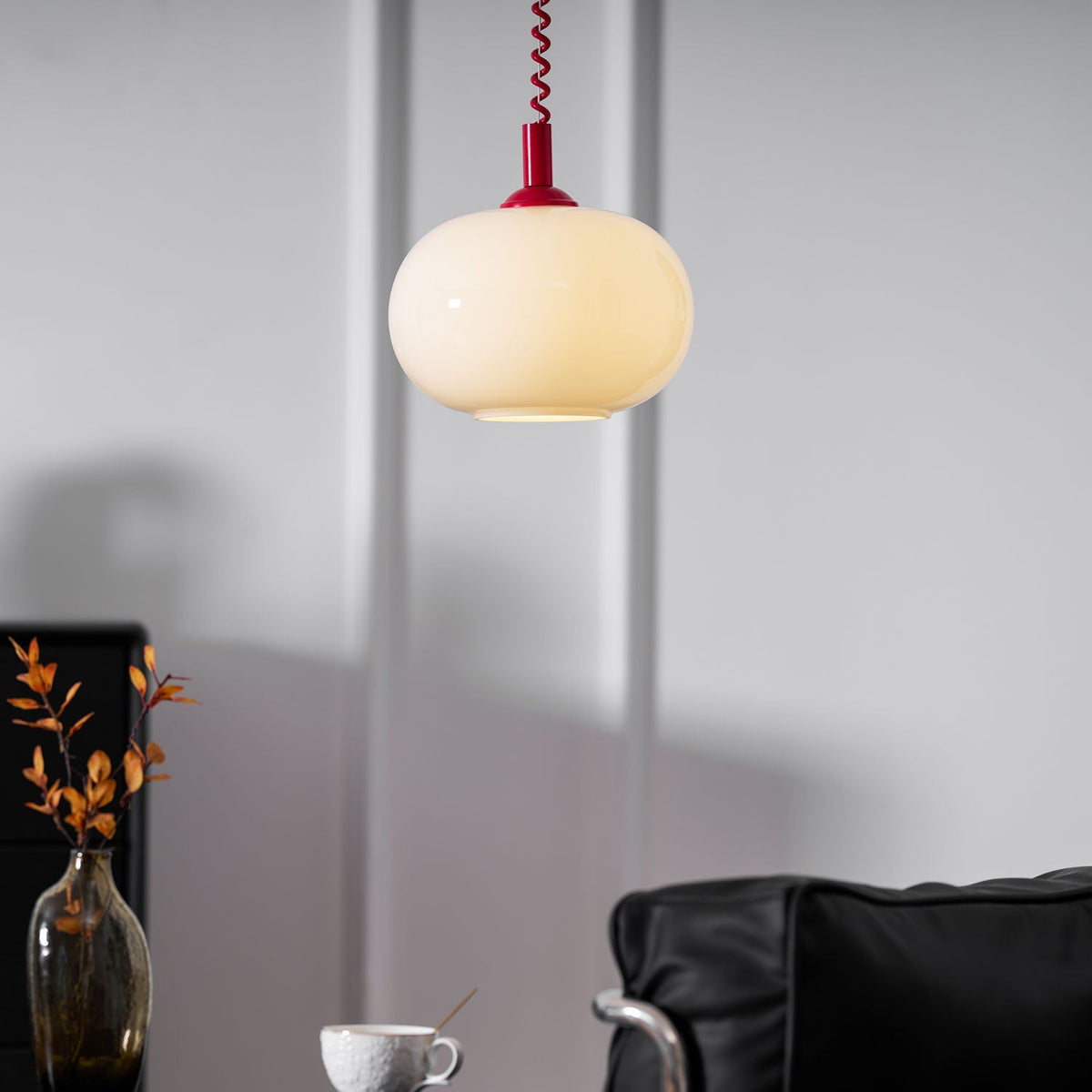 Close crop of this Clérachic pendant lit above a white panelled wall, a red cap and coil cable over the milky shade.