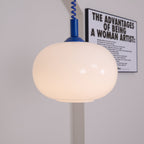 Close view of the rounded milky glass shade on this Clérachic pendant, with a blue cap and coil cable against a pale wall.