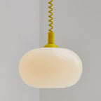 Close view of the yellow-capped Clérachic pendant, its milky glass shade glowing a soft cream under a yellow coil cable.