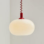 Close view of the red-capped Clérachic pendant lit, the milky shade glowing a warm cream against a pale grey wall.
