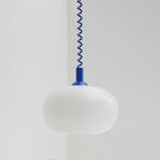 Unlit Clérachic pendant with a blue cap and blue coil cable, its white shade hanging in a pale grey corner.