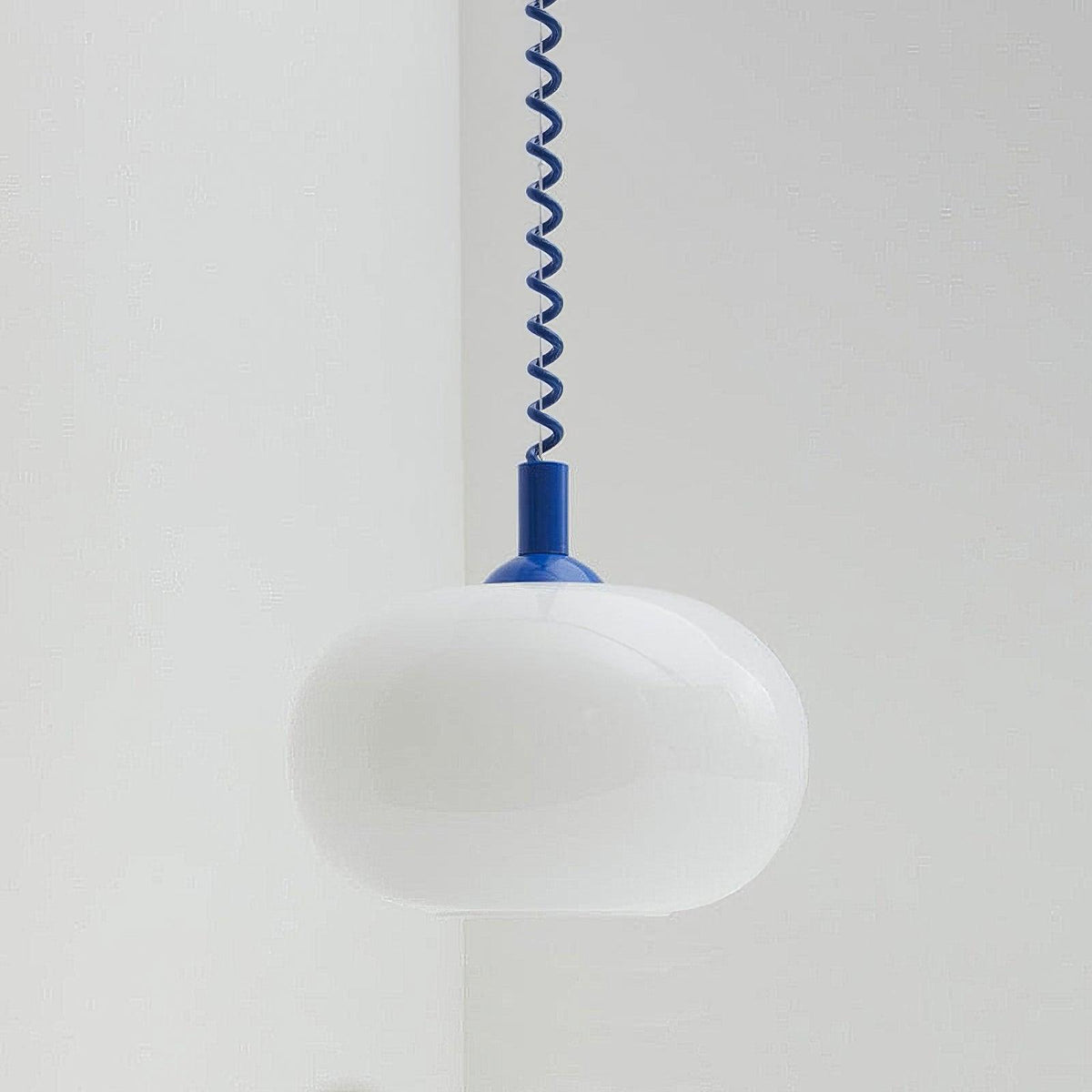 Unlit Clérachic pendant with a blue cap and blue coil cable, its white shade hanging in a pale grey corner.
