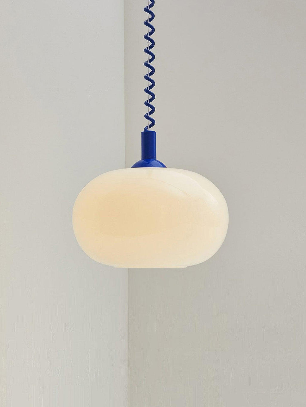 Blue-capped Clérachic pendant lit warm and centred against a pale corner, with the coil cable running straight up.