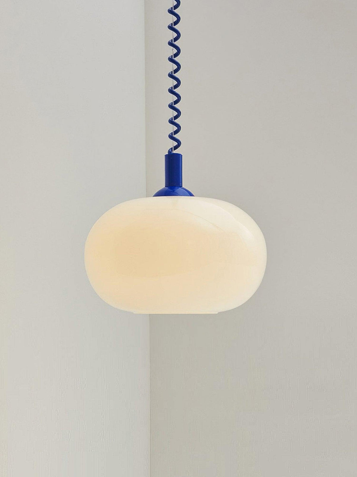 Blue-capped Clérachic pendant lit warm and centred against a pale corner, with the coil cable running straight up.