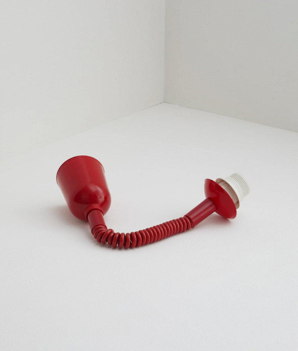 Red cap, stretch-coil cable and lamp holder of this Clérachic pendant laid on a white floor, with the glass shade removed.