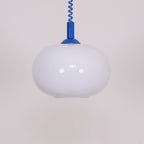 Close view of this Clérachic pendant, with a blue cap and cable, the white shade unlit and showing soft reflections.