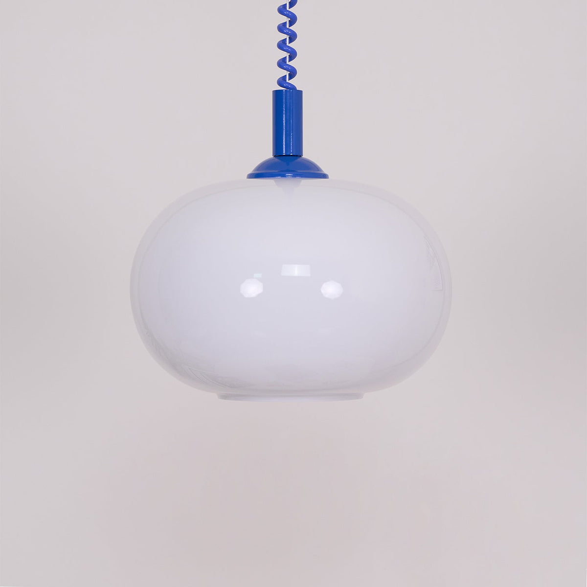 Close view of this Clérachic pendant, with a blue cap and cable, the white shade unlit and showing soft reflections.