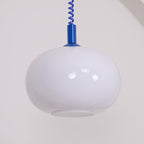 Large close view of the unlit white glass shade on this Clérachic pendant, with a blue cap and coil cable above it.