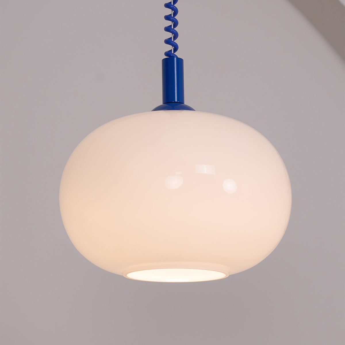 Close view of the blue-capped Clérachic pendant glowing a soft peach, its stretch-coil cable running up out of frame.