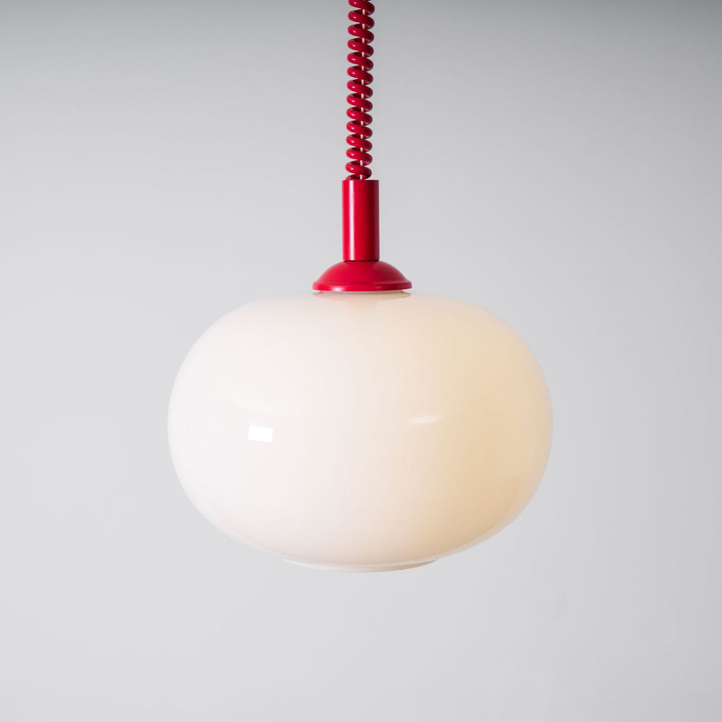 Red-capped Clérachic pendant with a glowing cream shade, seen close against a pale grey wall, with a red coil cable above.