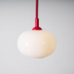 Red-capped Clérachic pendant with a glowing cream shade, seen close against a pale grey wall, with a red coil cable above.