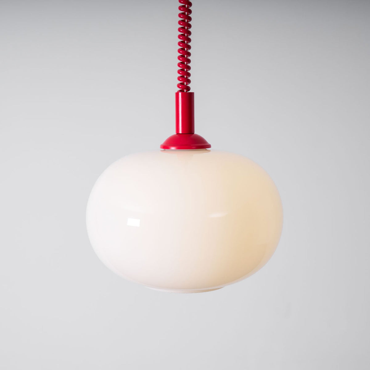 Red-capped Clérachic pendant with a glowing cream shade, seen close against a pale grey wall, with a red coil cable above.