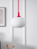 Close view of the white glass shade and red cap of this Clérachic pendant, with a framed picture at the edge of the wall.