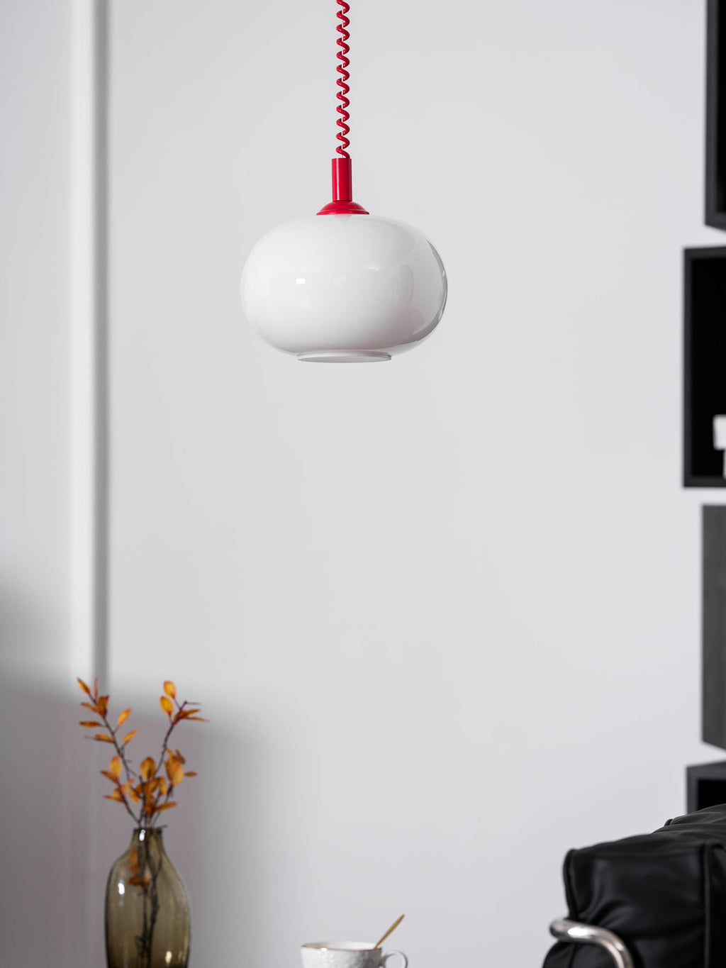 Unlit Clérachic pendant with a red cap on a white panelled wall, a vase of orange leaves and a chair below.