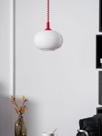 Unlit Clérachic pendant with a red cap on a white panelled wall, a vase of orange leaves and a chair below.