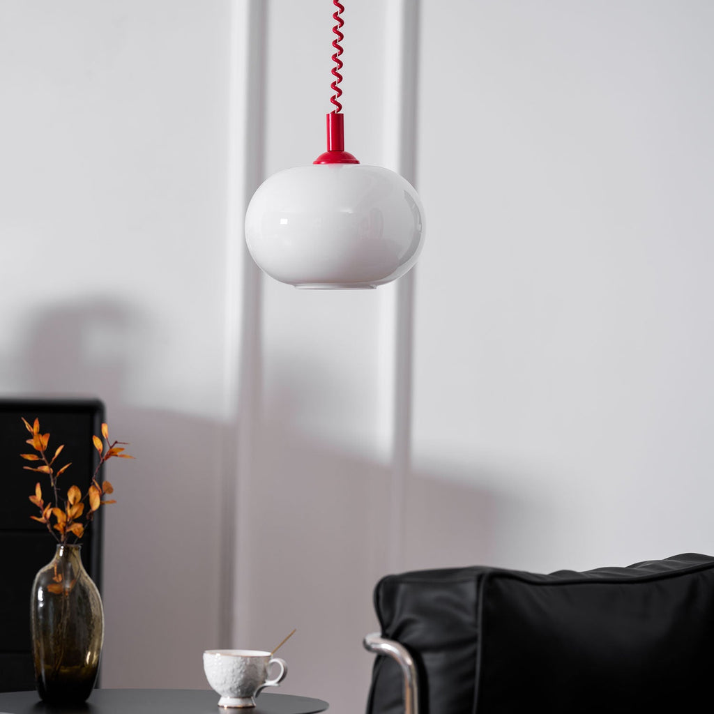This Clérachic pendant with a red cap hanging beside a black chair and a smoky glass vase with a cup on the table.