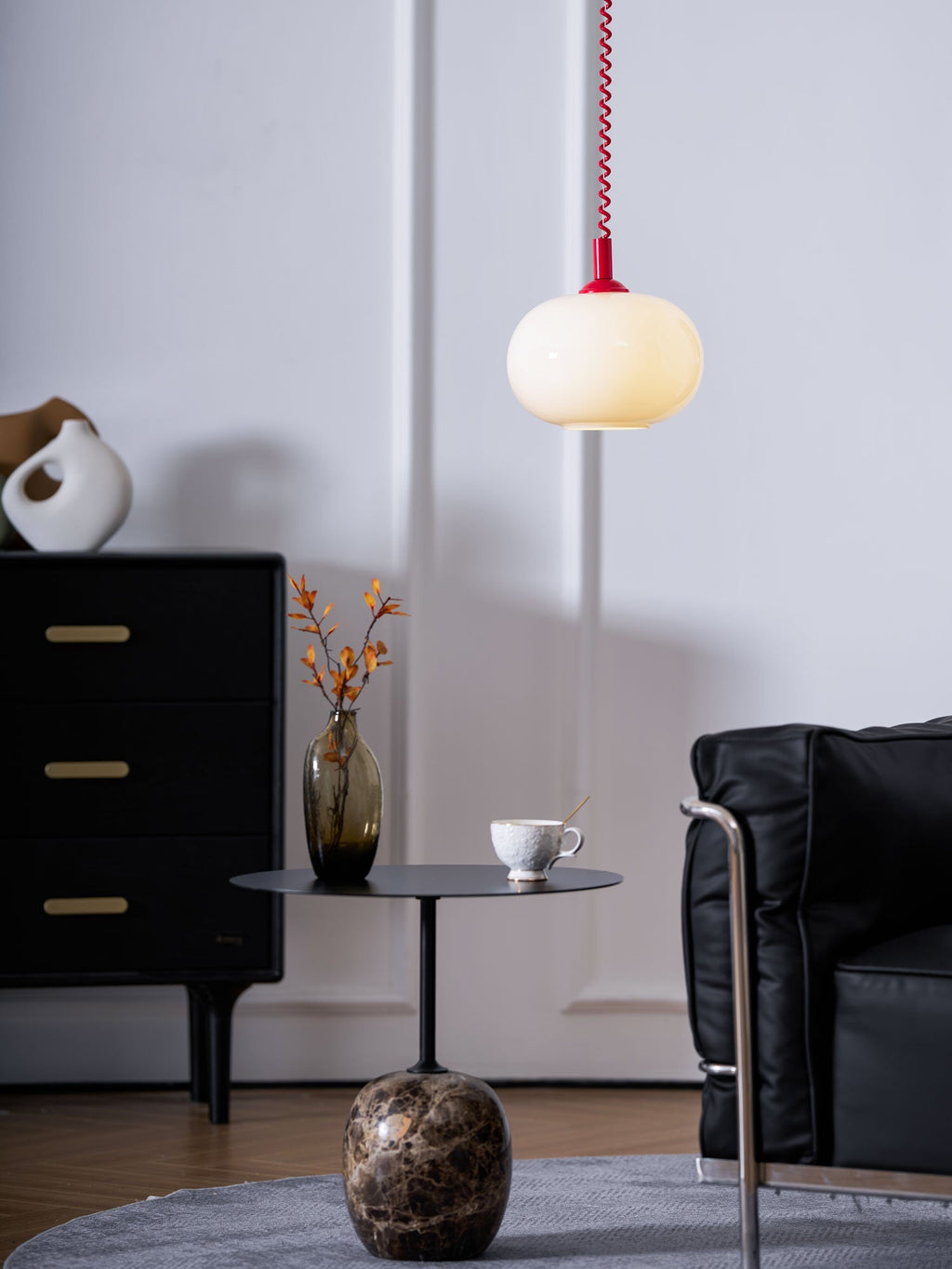 A lit Clérachic pendant with a red cap above a black side table, a marble base and a dark cabinet, in a living room.