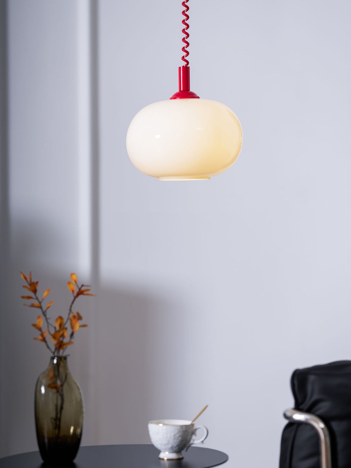 Red-capped Clérachic pendant glowing softly against a lilac-grey wall, with a vase of leaves and a cup below.