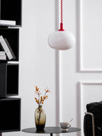 Clérachic pendant with a red cap and white shade hanging by a black shelving unit, a vase of orange leaves below.
