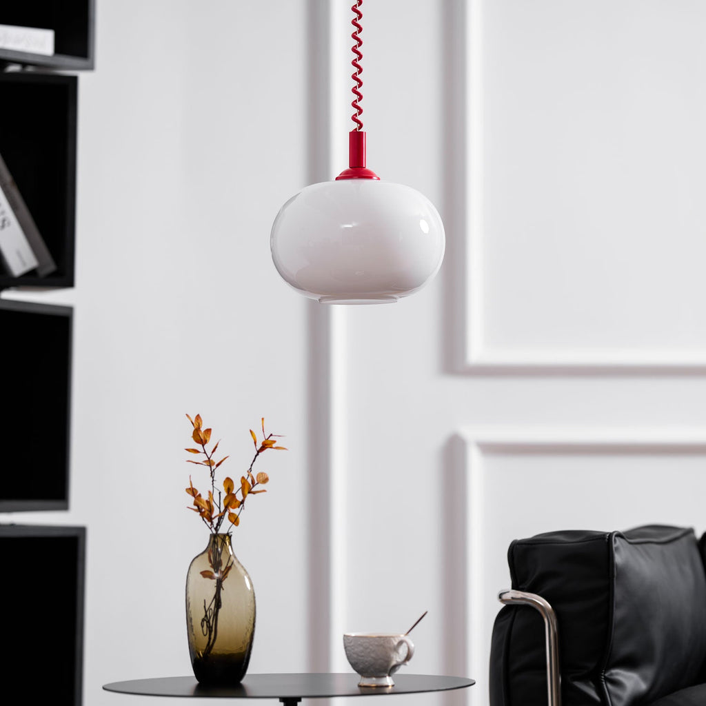 Unlit Clérachic pendant with a red cap hanging in front of a white panelled wall, a vase and a black armchair beneath.