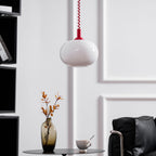 Unlit Clérachic pendant with a red cap hanging in front of a white panelled wall, a vase and a black armchair beneath.