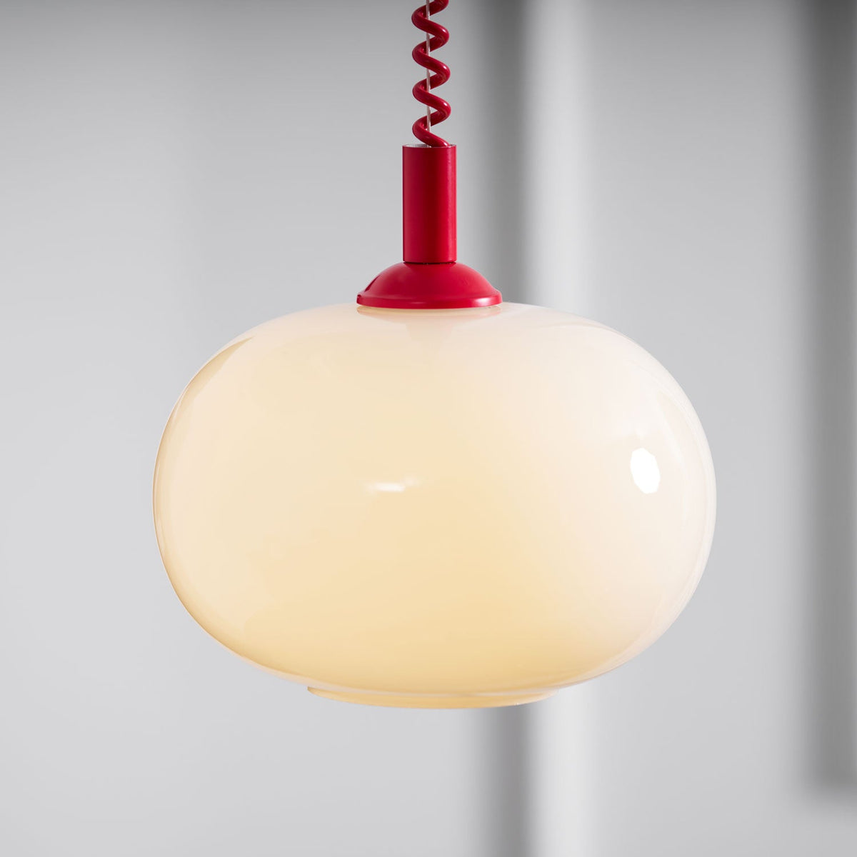Close view of the lit Clérachic pendant, its milky shade glowing warm cream under a red cap and coil cable.