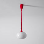 The red Clérachic pendant hanging from a red ceiling cap on a straight red cable, with a white glass shade against a grey wall.