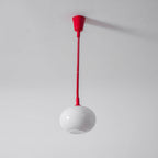 A Clérachic pendant with a red ceiling cap and straight red cable, its white shade hanging below with the opening visible.