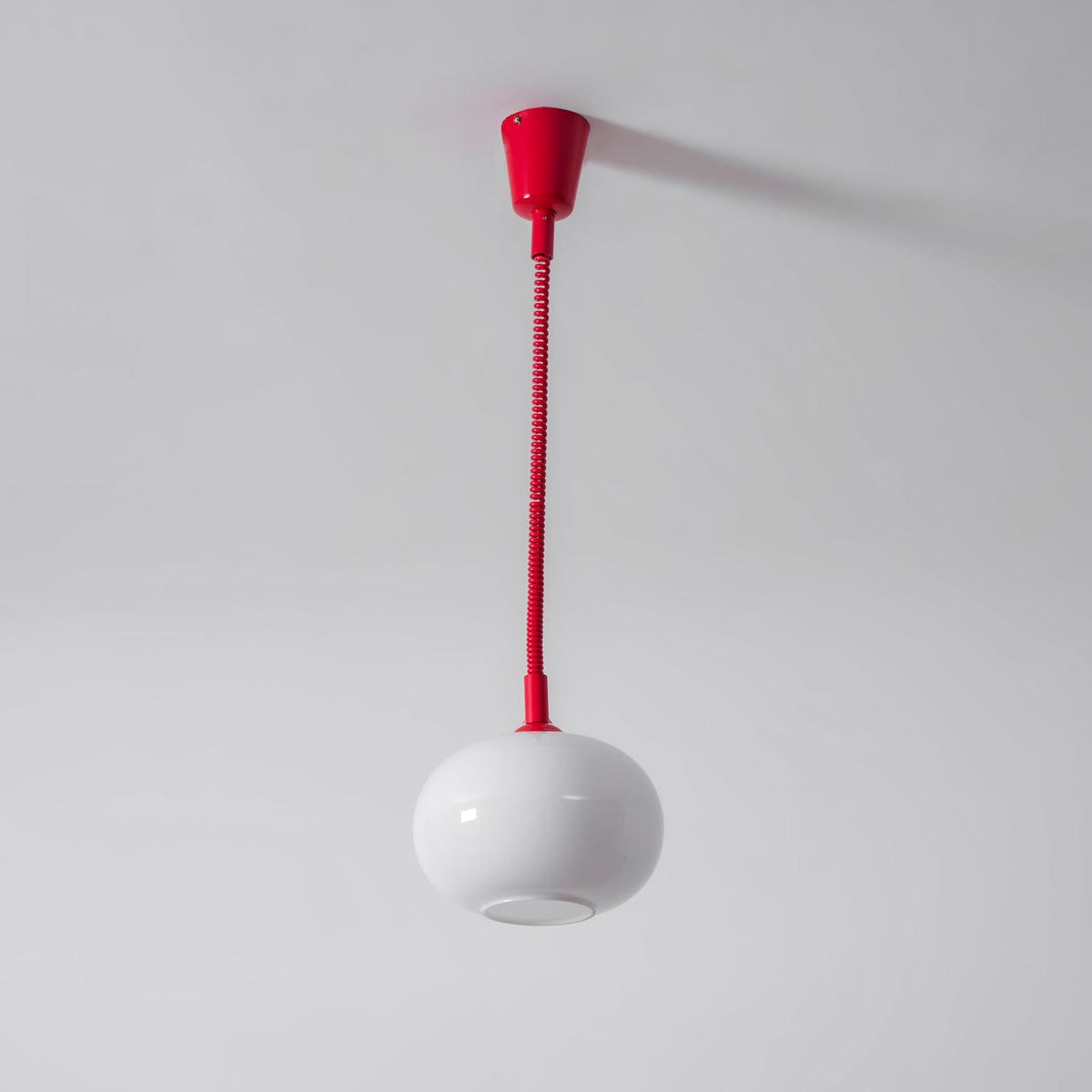 A Clérachic pendant with a red ceiling cap and straight red cable, its white shade hanging below with the opening visible.