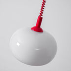 Close view of the white glass shade and red cap on this Clérachic pendant, seen from slightly below.