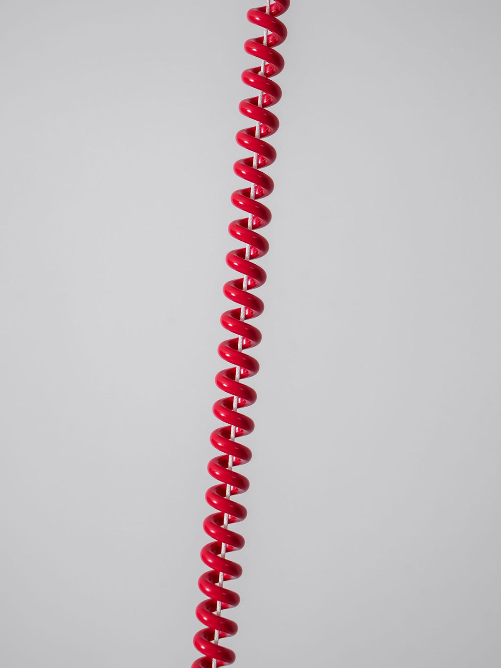 Close view of the red stretch-coil cable on this Clérachic pendant, hanging against a plain grey wall.