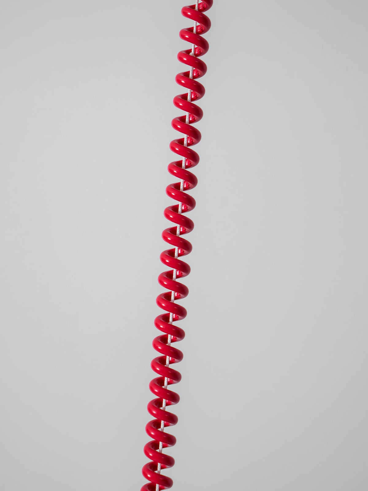 Close view of the red stretch-coil cable on this Clérachic pendant, hanging against a plain grey wall.