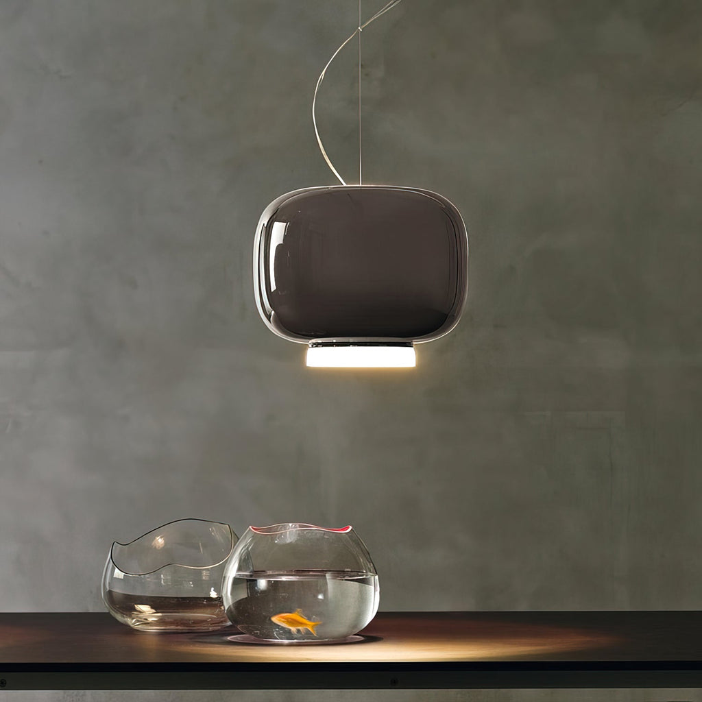 Rounded dark taupe-brown glass shade with a lit white base, a Clérachic pendant above a table with two glass fish bowls.
