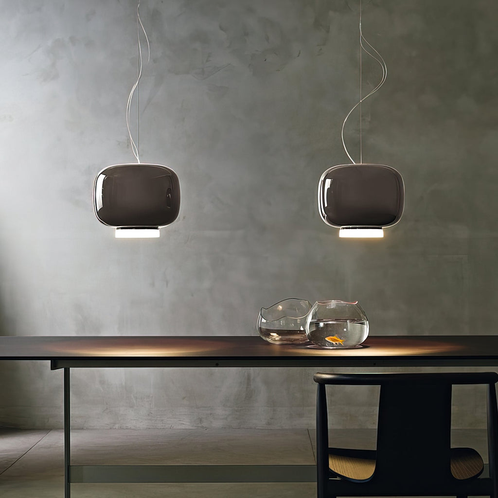 Pair of dark taupe glass pendants from Clérachic against a concrete-look wall, hung over a dark table with glass bowls.