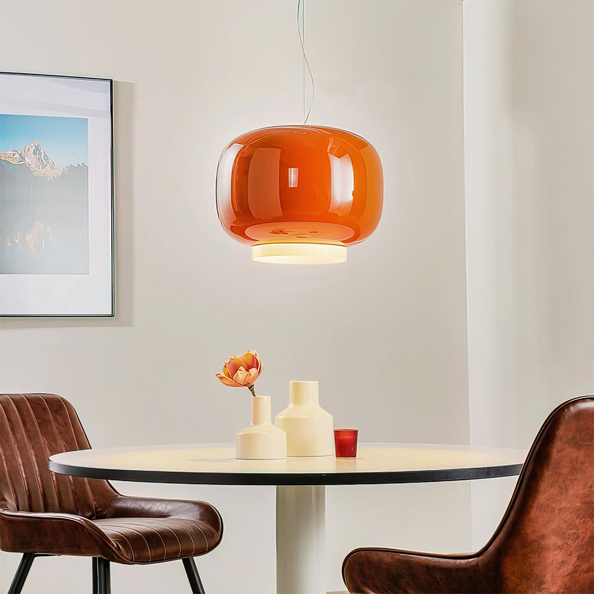 Glossy orange glass pendant above a small round table with cream vases, a Clérachic light beside leather chairs.