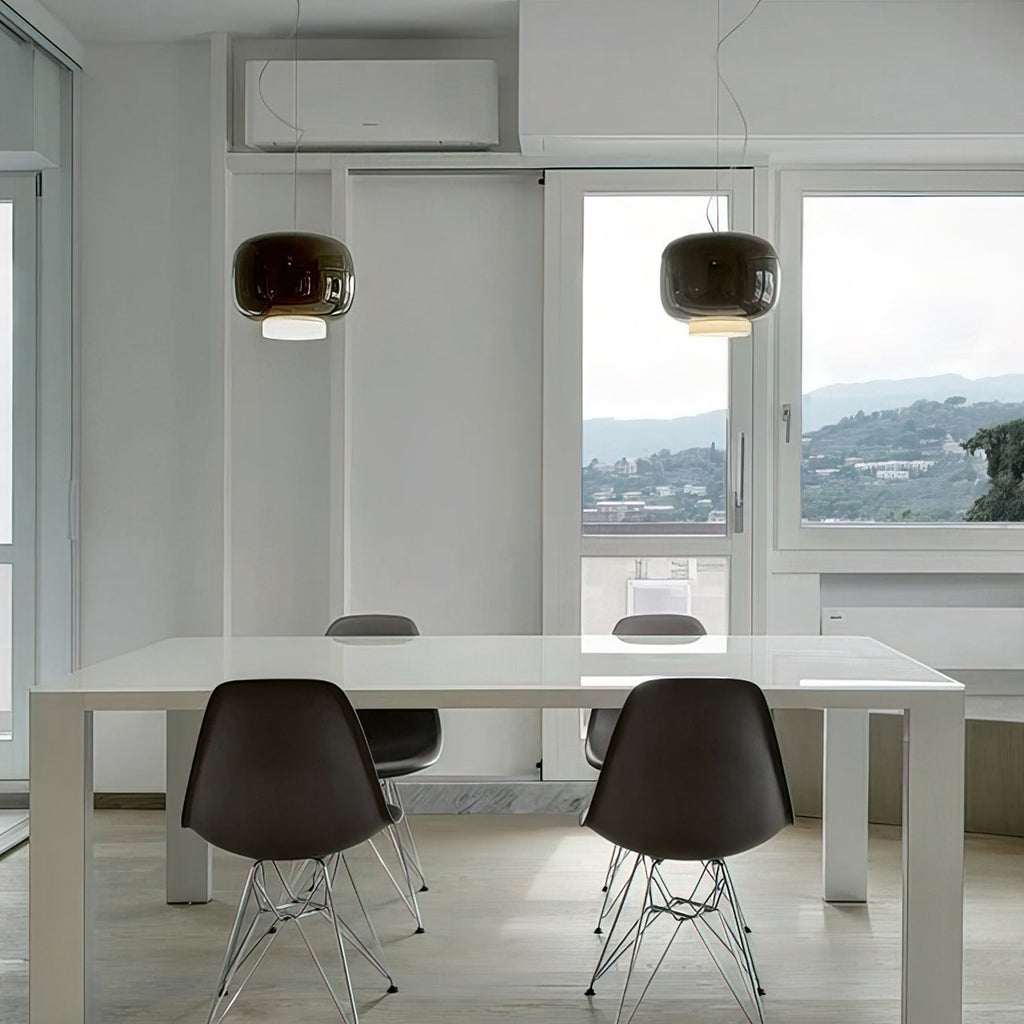 Two dark glass pendants from Clérachic hang in a bright room with a white table, black chairs and a window view of hills.