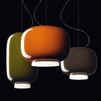 Orange, olive-green and dark taupe glass pendants from Clérachic against a black backdrop, their white bases lit.