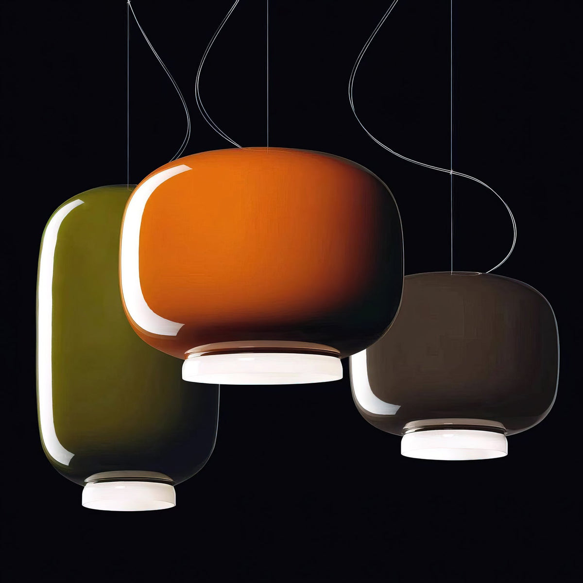 Orange, olive-green and dark taupe glass pendants from Clérachic against a black backdrop, their white bases lit.