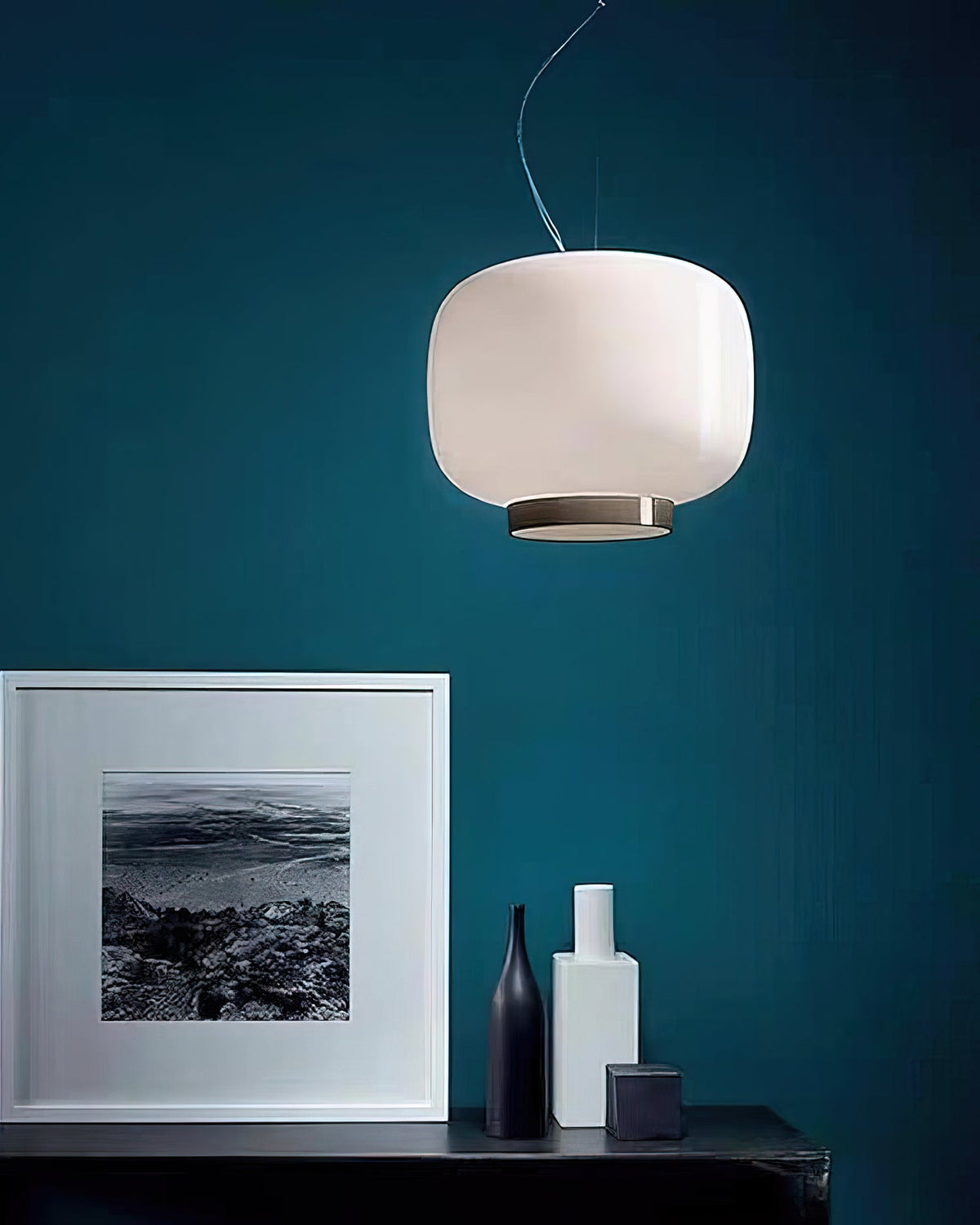 White glass lantern pendant against a deep teal wall, a Clérachic light above a framed print and a few vases.