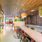 Orange and green glass pendants from Clérachic hang above a long wooden counter in a spacious room with a slatted ceiling.
