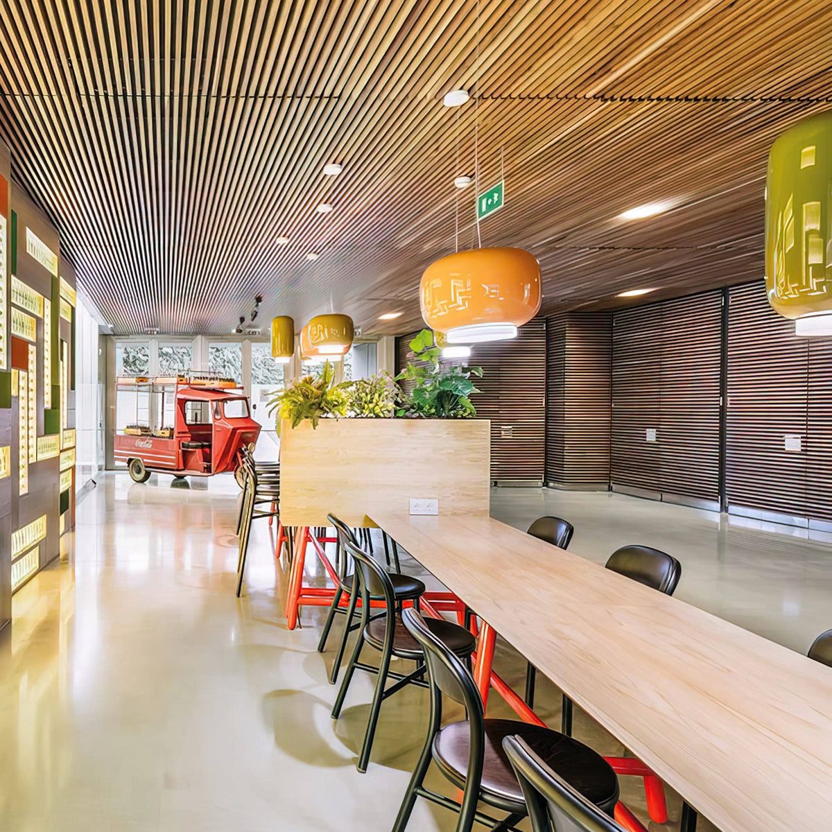 Orange and green glass pendants from Clérachic hang above a long wooden counter in a spacious room with a slatted ceiling.