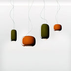 Four Clérachic glass pendants in green and orange hang on trailing cables at different heights against a soft white backdrop.