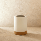 The Clérachic table lamp, a single frosted cylinder lamp with a light wood base, glowing softly against a wall.