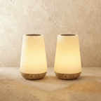 A pair of Clérachic table lamps in their tapered form, two frosted shades glowing above light wood bases.