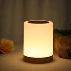 Clérachic's table lamp glowing warmly on a dark wood base beside a flower and soft fabric in a cozy scene.