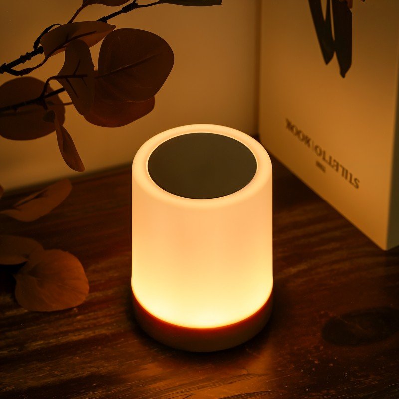 Clérachic's table lamp glowing warmly on a dark wood tabletop, framed by dried leaves and a paper gift box.