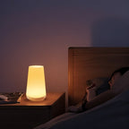 Clérachic's table lamp glowing warm on a bedside table beside a person sleeping in a dim bedroom at night.