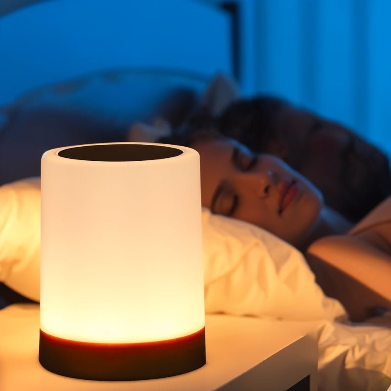 Clérachic's table lamp glowing warm on a nightstand beside a person sleeping under blue bedroom light.