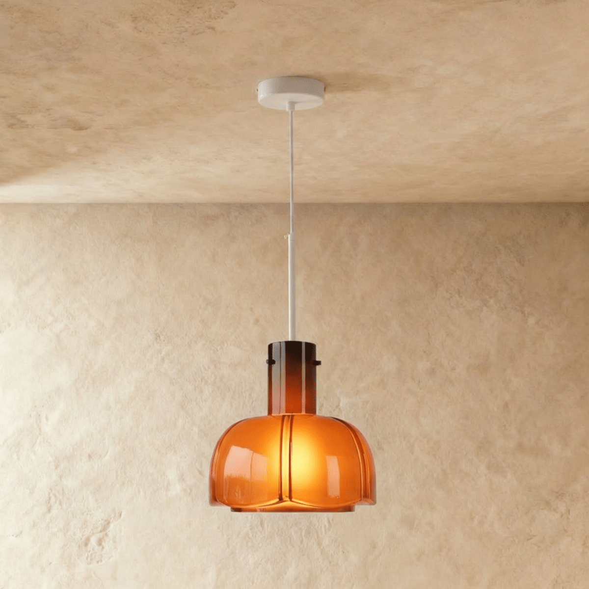 Clérachic rounded amber glass pendant, glowing warm, hung from a slim white stem and canopy against a limewashed wall.